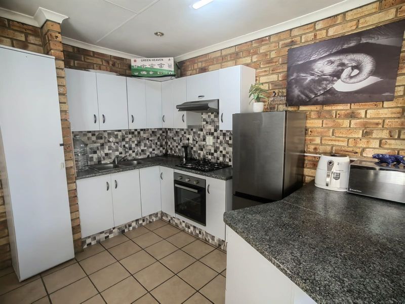 A functional kitchen featuring white cabinetry, granite countertops, a built-in oven with gas hob, and distinctive exposed brick walls with tiled flooring.
