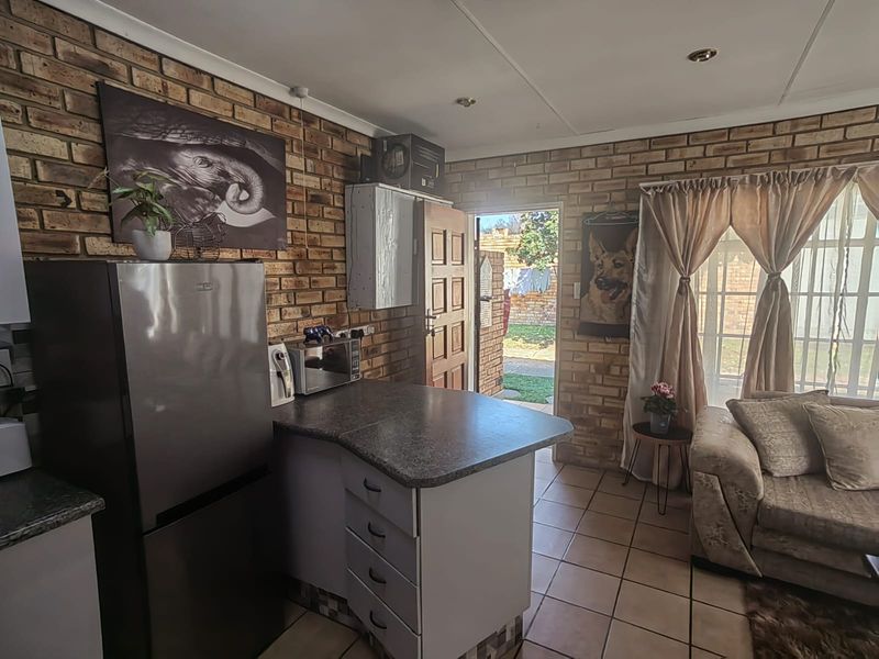 Open-plan living and kitchen area featuring exposed brick walls, tiled flooring, and direct access to the rear garden through a sliding glass door.