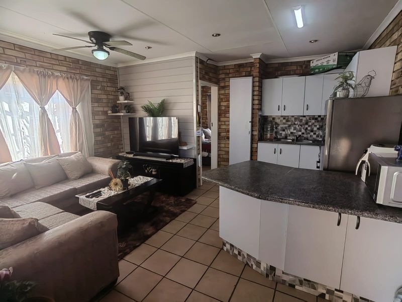 Open-plan living and kitchen area featuring exposed brick walls, tiled flooring, and a functional kitchen with granite countertops and mosaic backsplash.