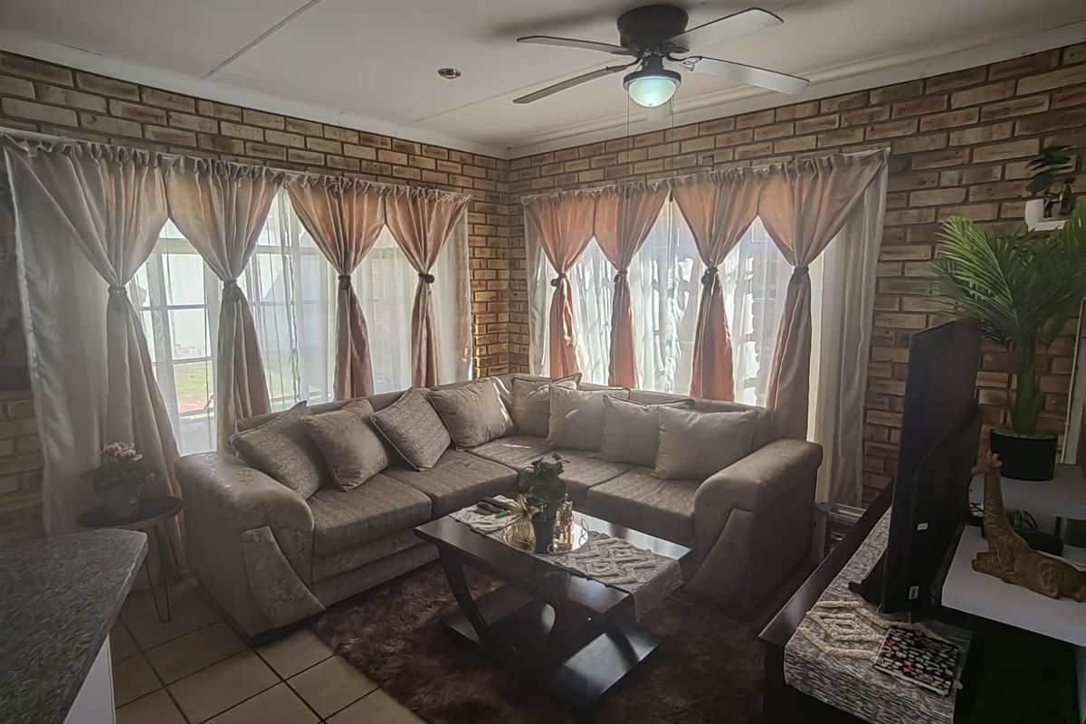 A cozy living room featuring exposed brick walls, tiled flooring, and a ceiling fan, offering a warm and textured aesthetic.