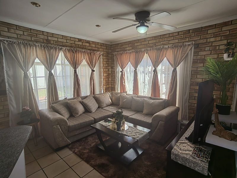 A cozy living room featuring exposed brick walls, tiled flooring, and a ceiling fan, offering a warm and textured aesthetic.