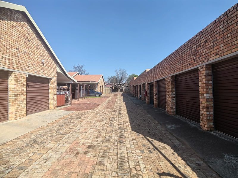 A view of a paved driveway lined with multiple facebrick garage units in a townhouse complex.