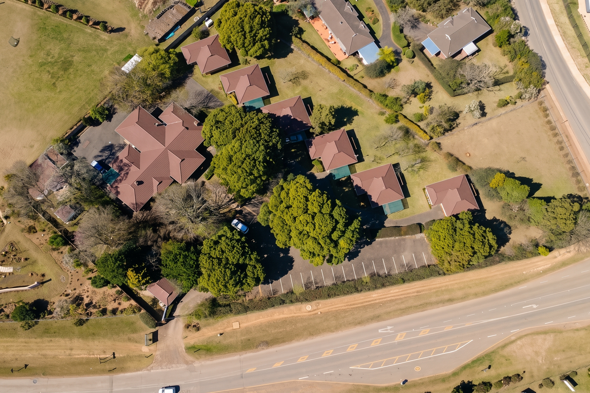 Aerial view of a property complex featuring multiple buildings with tiled roofs, extensive landscaped grounds, and a dedicated paved parking area.