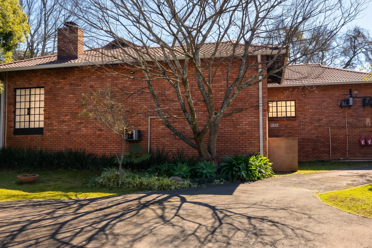 A view of the rear brick facade of the house, featuring a tiled roof, chimney, and an adjacent asphalt driveway.