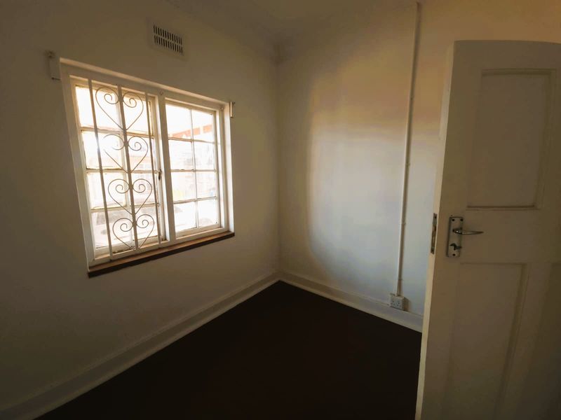 An empty bedroom featuring white walls, dark flooring, a window with security bars, and visible surface-mounted electrical conduit.