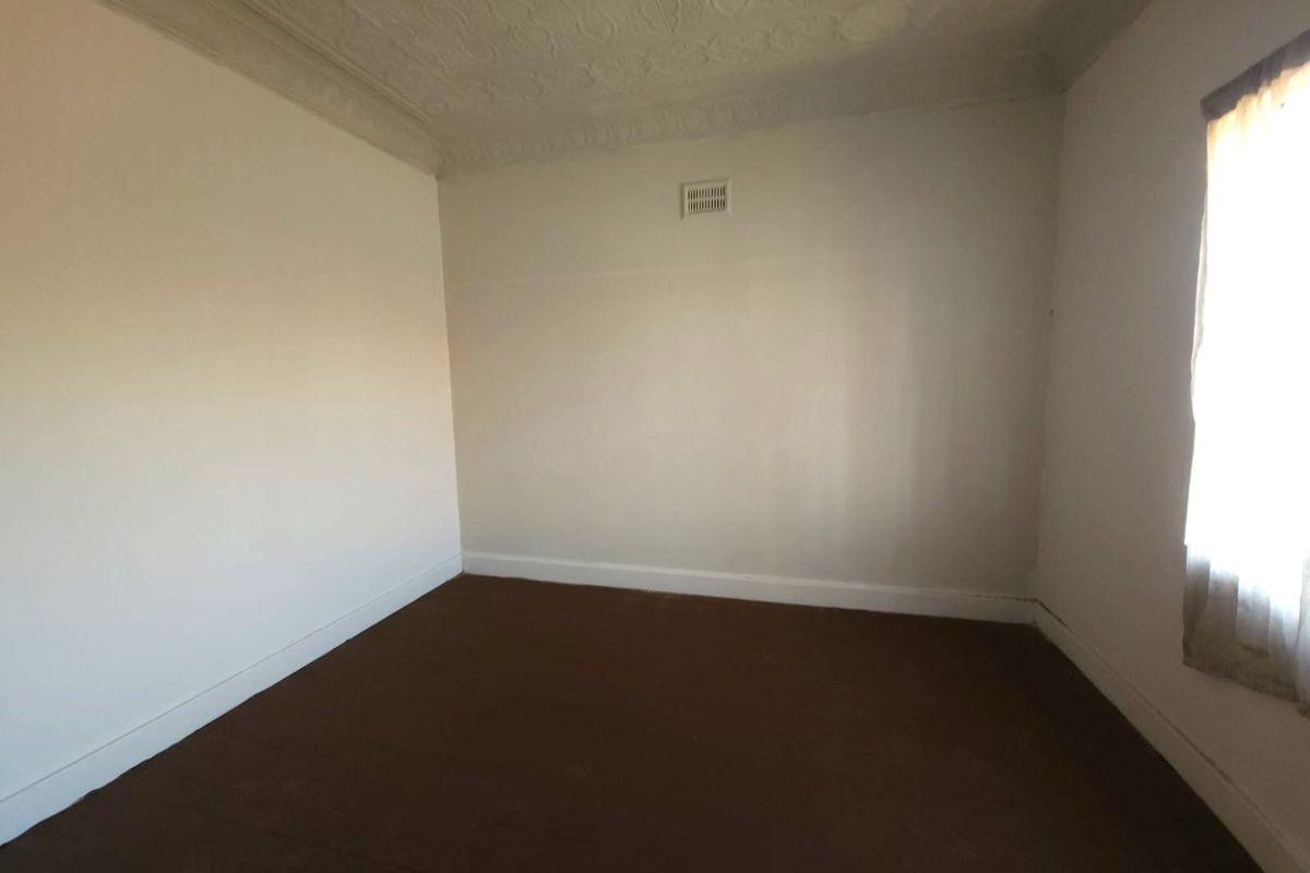 An empty bedroom featuring a decorative ceiling rose, ventilation grille, and neutral wall finishes, ready for a fresh update.