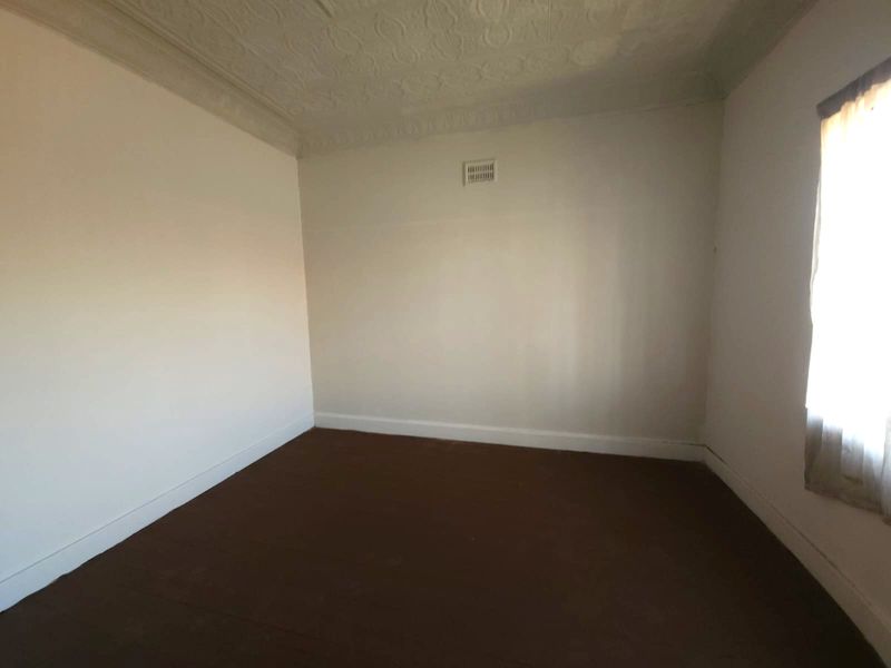 An empty bedroom featuring a decorative ceiling rose, ventilation grille, and neutral wall finishes, ready for a fresh update.