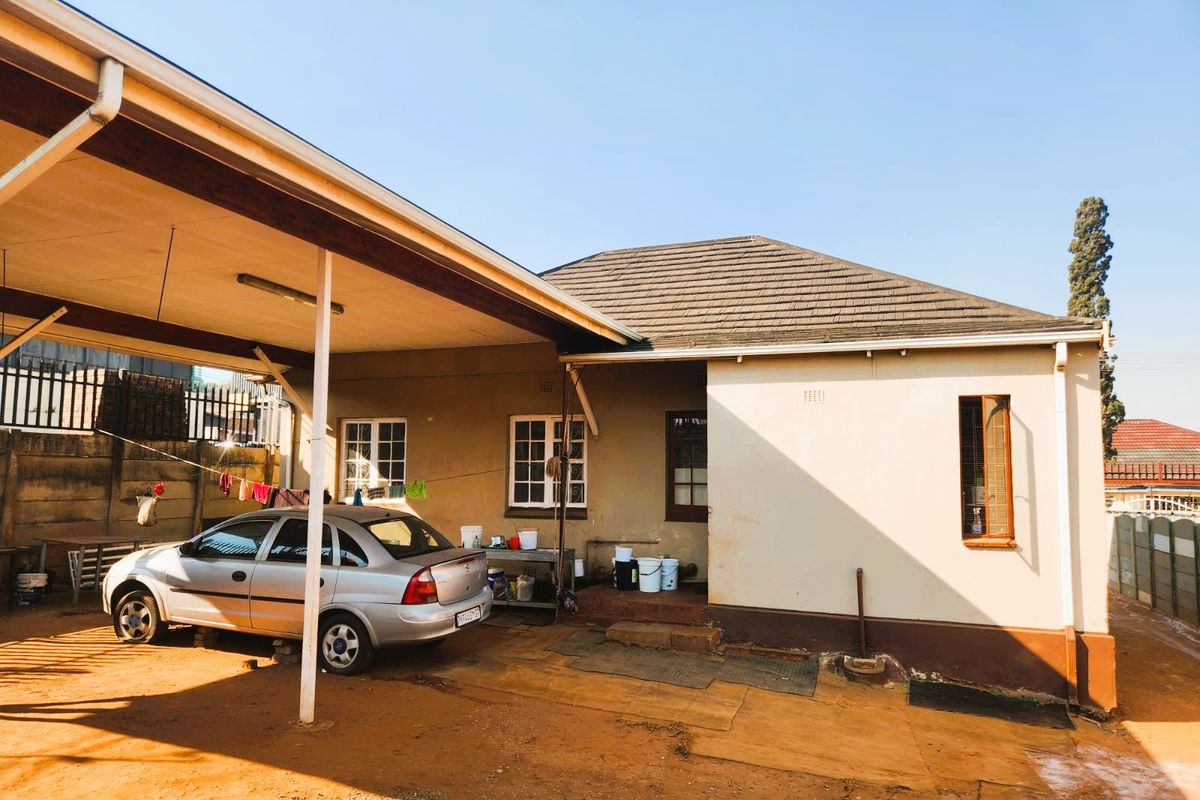 Rear exterior view of the property featuring a covered carport area, tiled roof, and concrete boundary walling.