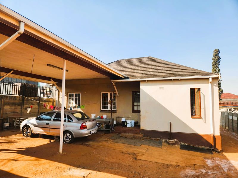 Rear exterior view of the property featuring a covered carport area, tiled roof, and concrete boundary walling.