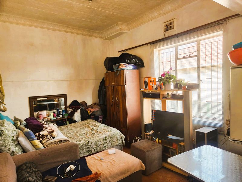 A bedroom featuring a steel window frame, decorative ceiling cornice, and textured ceiling, currently requiring cosmetic updates to the wall and ceiling finishes.