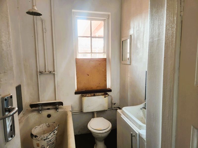 A dated bathroom featuring a bathtub, toilet, and vanity basin, requiring significant renovation and cosmetic updates to restore functionality and appeal.