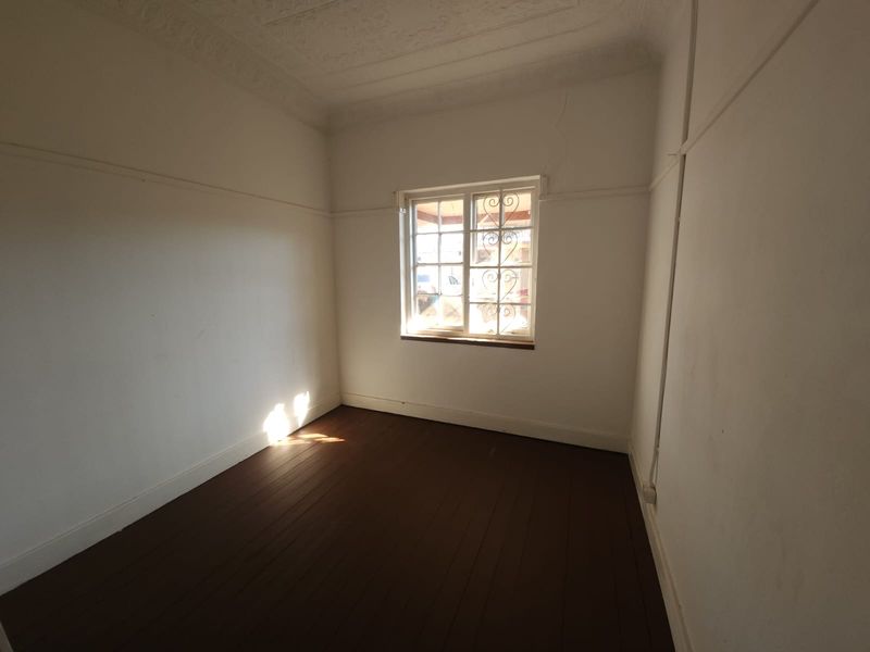 An empty bedroom featuring original timber flooring, decorative ceiling details, and security bars on the window. The space requires minor wall repairs.