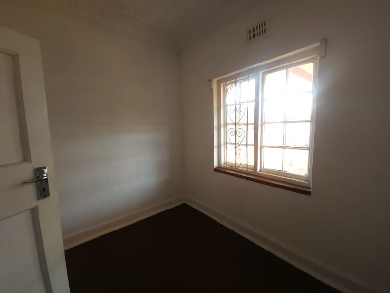 An empty bedroom featuring white walls, dark flooring, and a window fitted with a decorative security gate.