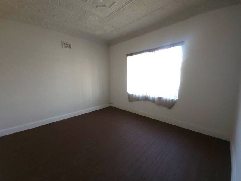 An empty bedroom featuring original pressed metal ceilings and dark timber flooring, offering a blank canvas for renovation.