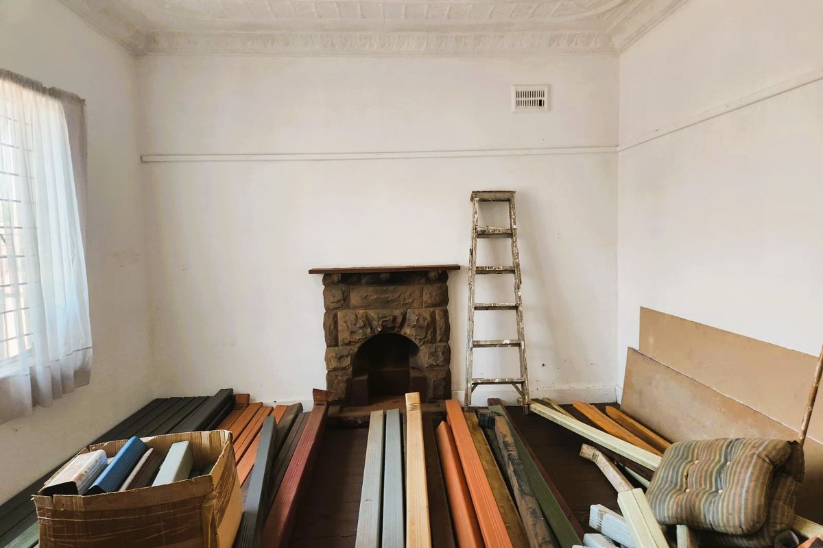 A vacant living room featuring a character stone fireplace, decorative ceiling, and original timber flooring, currently used for storage.