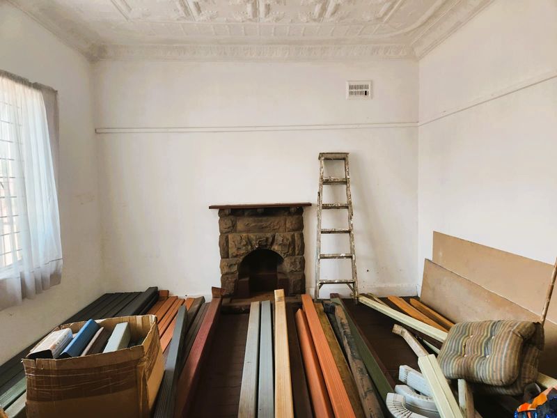 A vacant living room featuring a character stone fireplace, decorative ceiling, and original timber flooring, currently used for storage.