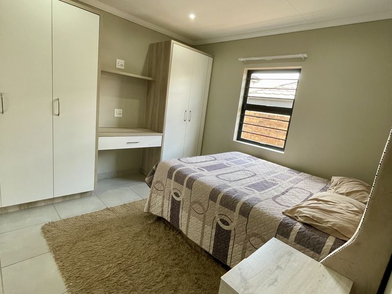 A well-maintained bedroom featuring neutral wall tones, tiled flooring, recessed lighting, and integrated built-in cupboards with a matching study desk.