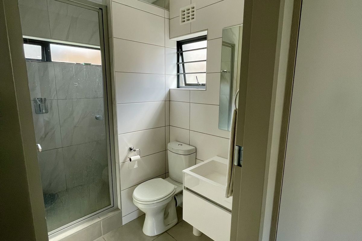 A clean, modern bathroom featuring a glass-enclosed shower, wall-mounted vanity basin, and neutral floor-to-ceiling tiling.