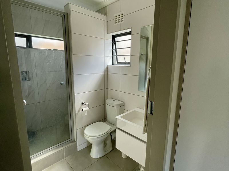 A clean, modern bathroom featuring a glass-enclosed shower, wall-mounted vanity basin, and neutral floor-to-ceiling tiling.
