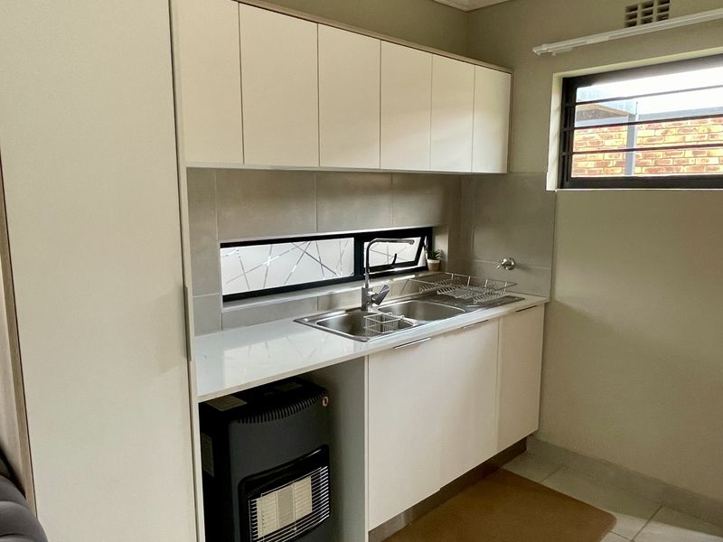 A clean and functional scullery featuring white built-in cabinetry, a stainless steel double sink, tiled splashbacks, and tiled flooring.