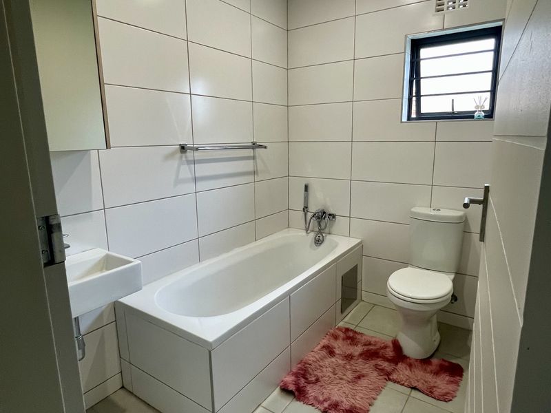 A clean, modern bathroom featuring white wall tiles, a built-in bathtub, a wall-mounted basin, and a standard toilet.