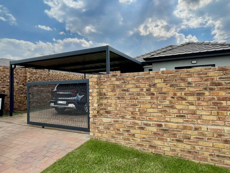 Front exterior view featuring a modern metal carport, paved driveway, and a well-maintained brick boundary wall with a secure sliding gate.