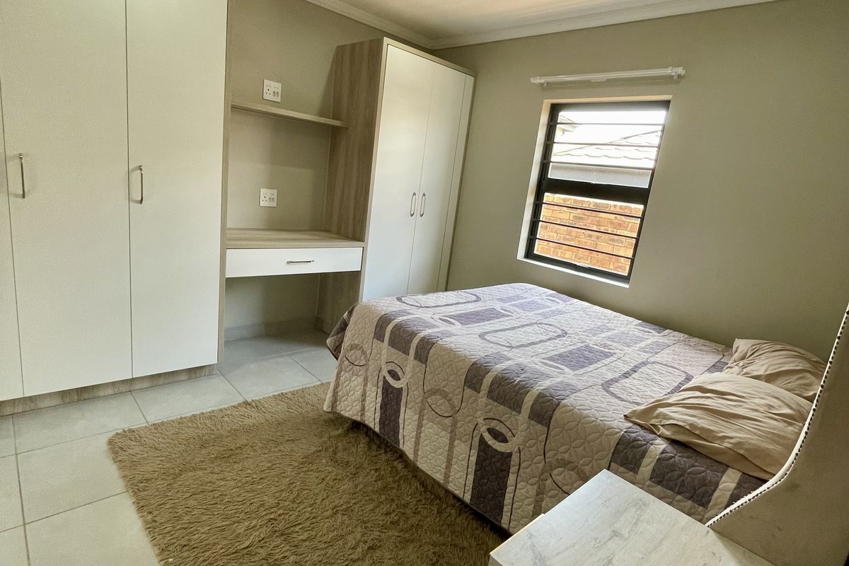 A well-maintained bedroom featuring neutral tiled flooring, built-in cupboards with an integrated desk, and recessed downlighting.