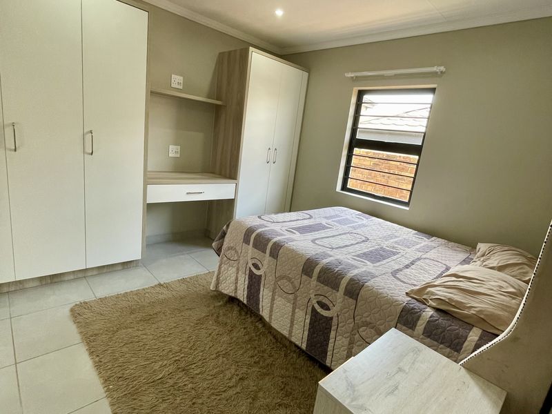A well-maintained bedroom featuring neutral tiled flooring, built-in cupboards with an integrated desk, and recessed downlighting.