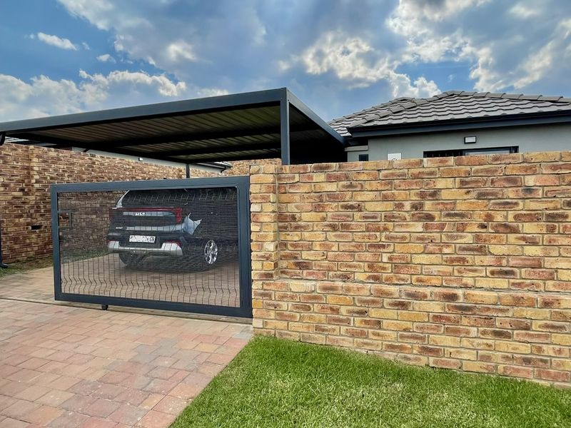 Front exterior view featuring a modern metal carport, secure sliding gate, and a well-maintained brick boundary wall with paved driveway.