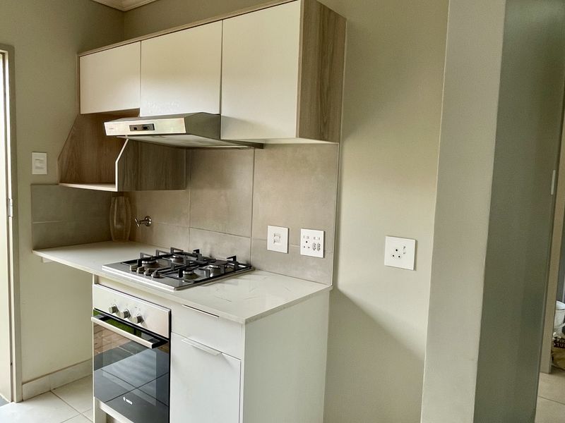 A compact, modern kitchen featuring built-in cabinetry, a gas hob, an integrated oven, and a neutral tiled backsplash.