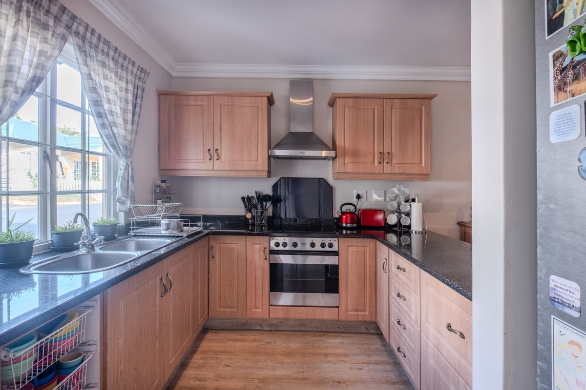 A functional kitchen featuring wooden cabinetry, granite countertops, a stainless steel oven with extractor fan, and a double bowl sink under a window.