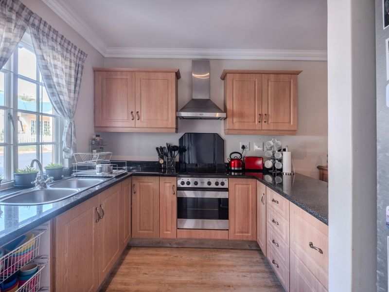 A functional kitchen featuring wooden cabinetry, granite countertops, a stainless steel oven with extractor fan, and a double bowl sink under a window.