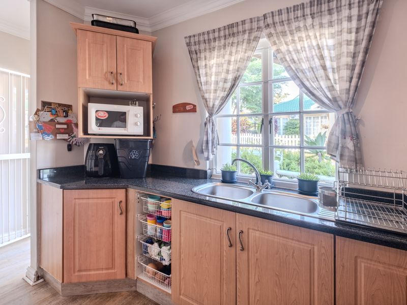 A functional kitchen area featuring light wood-finish cabinetry, dark granite countertops, and a double stainless steel sink overlooking the garden.