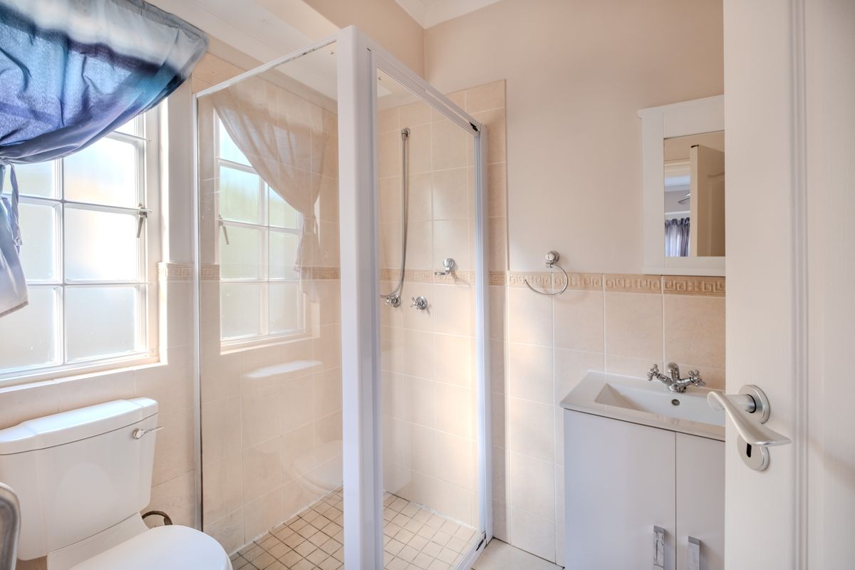 A functional bathroom featuring a shower enclosure, vanity basin, and toilet with neutral wall tiling and natural light from the window.
