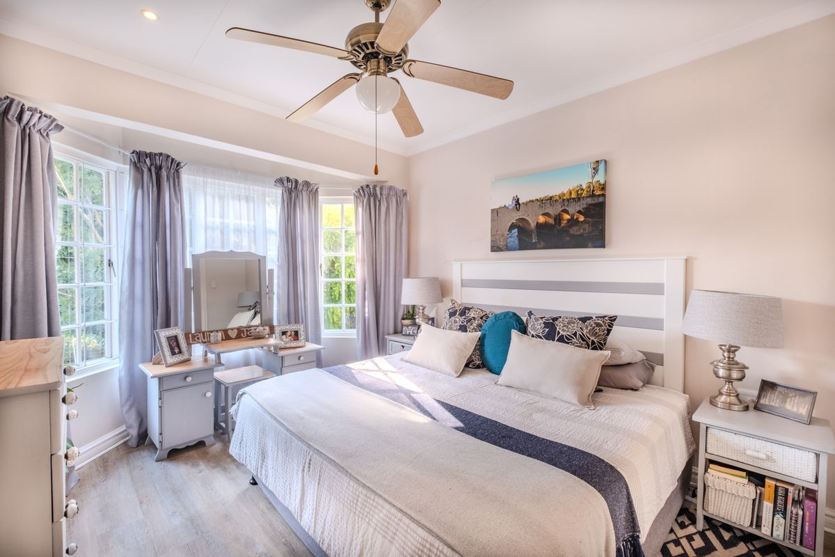 A well-maintained bedroom featuring a ceiling fan, bay windows providing natural light, and modern laminate flooring.