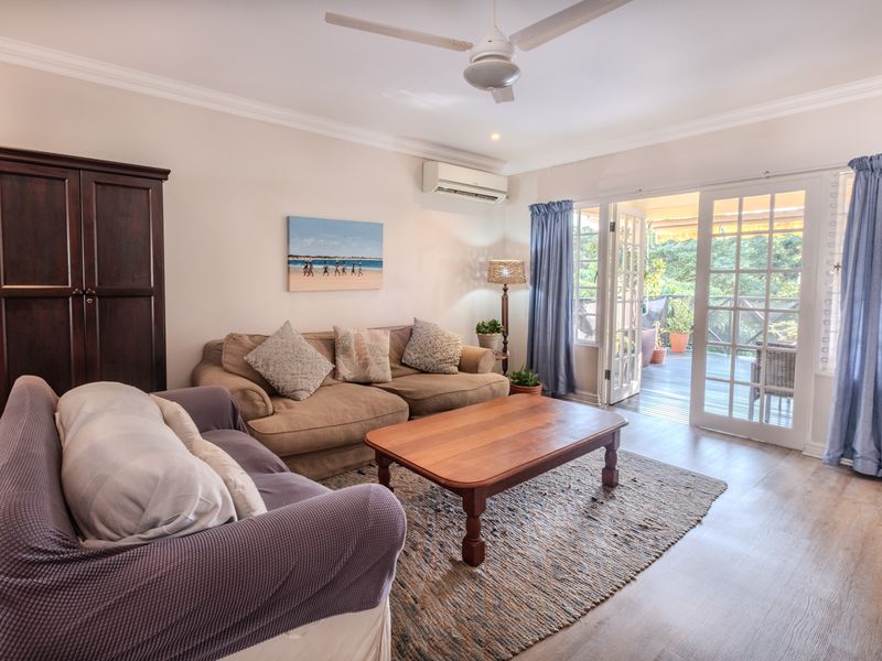 A bright living room featuring laminate flooring, a ceiling fan, split-system air conditioning, and direct access to an outdoor patio through glass french doors.
