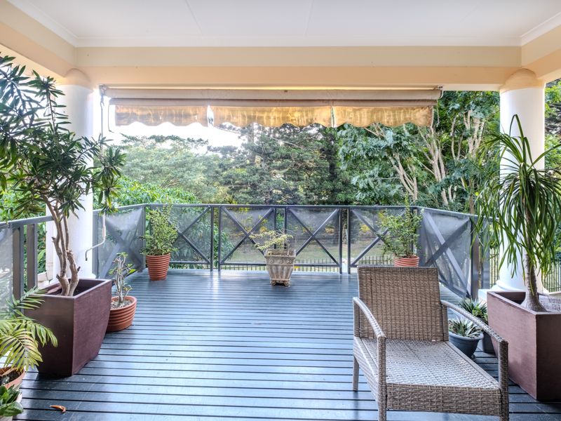 A covered balcony featuring timber decking, a retractable awning, and a metal balustrade, offering a pleasant outdoor space with garden views.