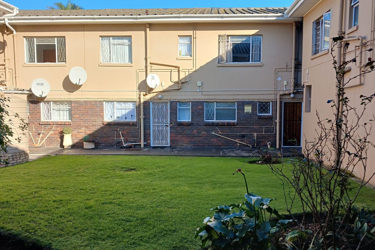 Rear view of the apartment complex featuring a shared lawn area, brick and plaster facade, and multiple window access points.