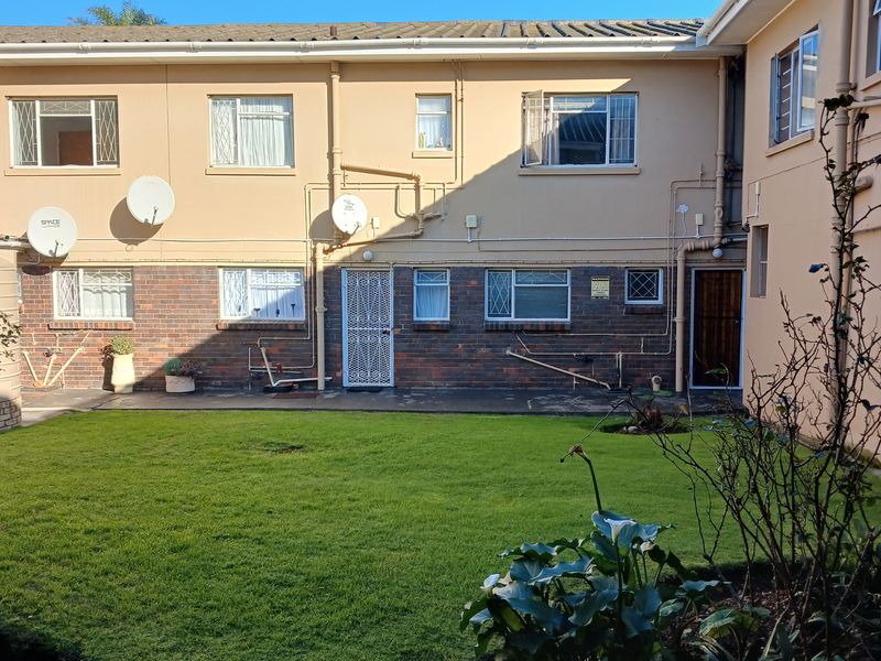 Rear view of the apartment complex featuring a shared lawn area, brick and plaster facade, and multiple window access points.