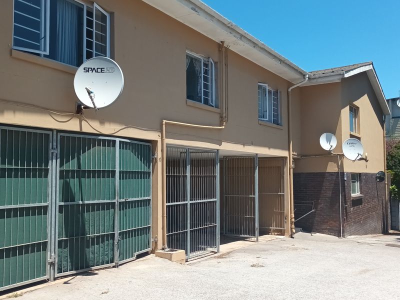 Exterior view of an apartment building featuring metal security gates, satellite dishes, and a paved driveway area.