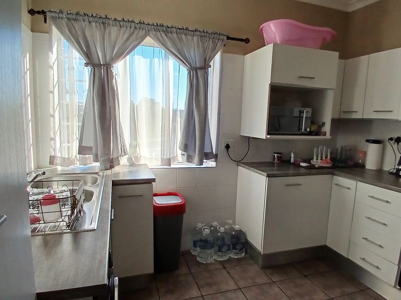 A functional kitchen featuring white built-in cabinetry, laminate countertops, a stainless steel sink, and tiled flooring with a window providing natural light.