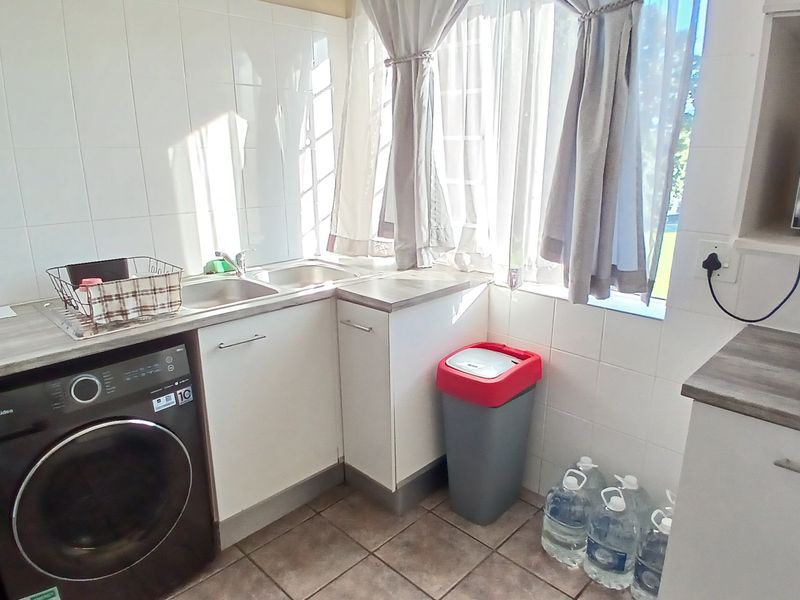 A functional laundry area featuring a double sink, tiled splashback, laminate countertops, and built-in cabinetry with tiled flooring.