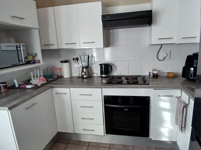 A functional kitchen featuring white cabinetry, a laminate countertop, built-in oven, electric hob, and a tiled backsplash.