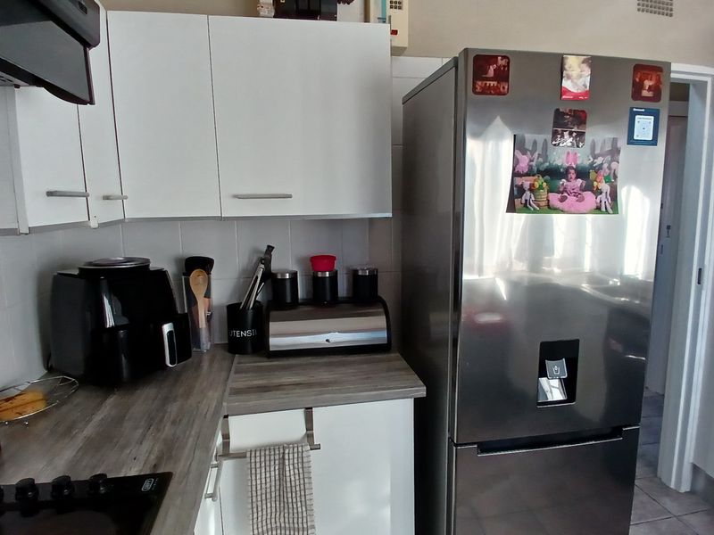 A functional kitchen featuring white cabinetry, a wood-look laminate countertop, tiled backsplash, and a built-in electric hob with an extractor fan.