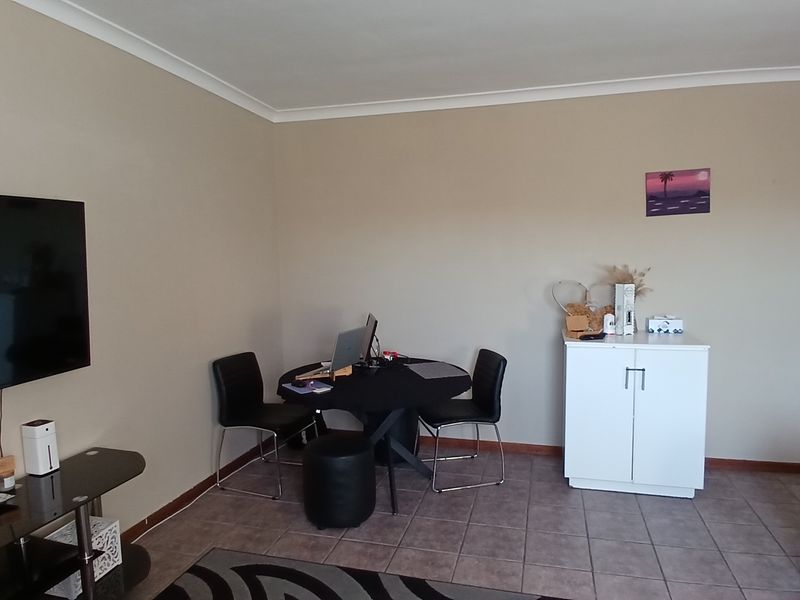A living area featuring neutral wall tones, tiled flooring, and coved ceiling detailing, providing a functional space for daily use.