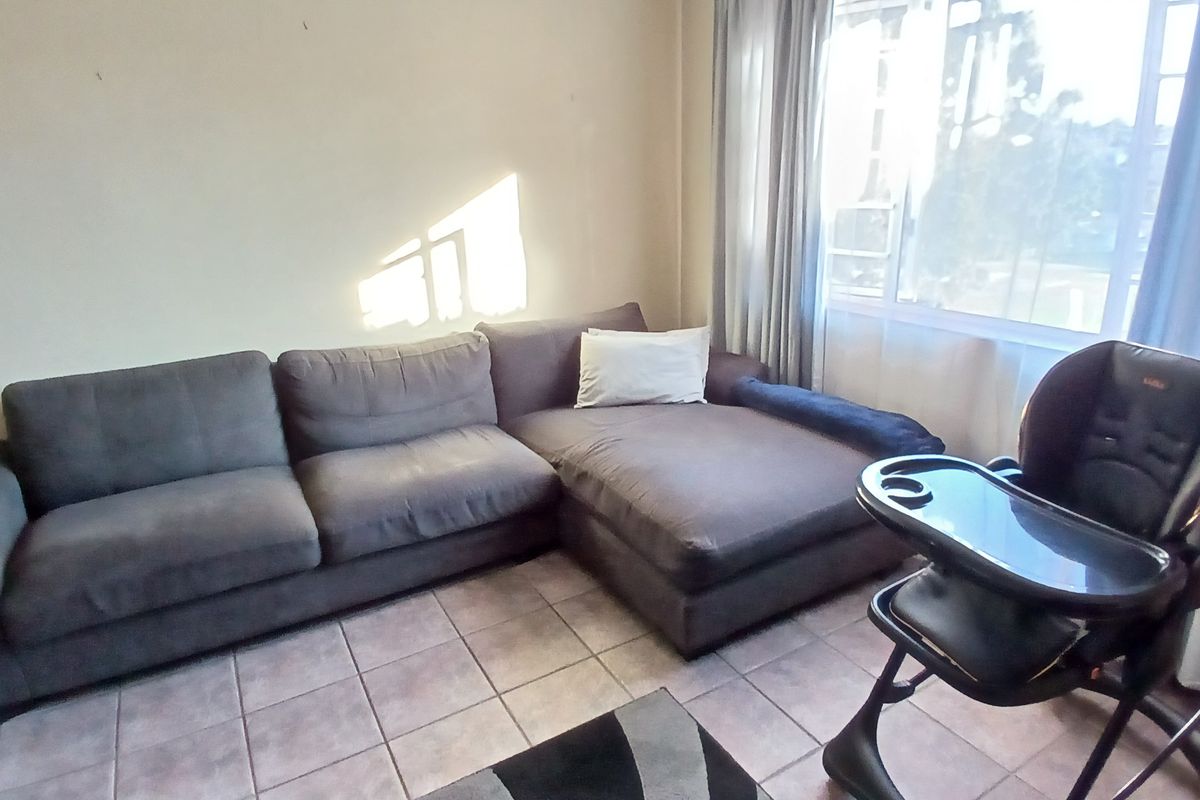 A living room area featuring tiled flooring and a large window, providing natural light to the space.