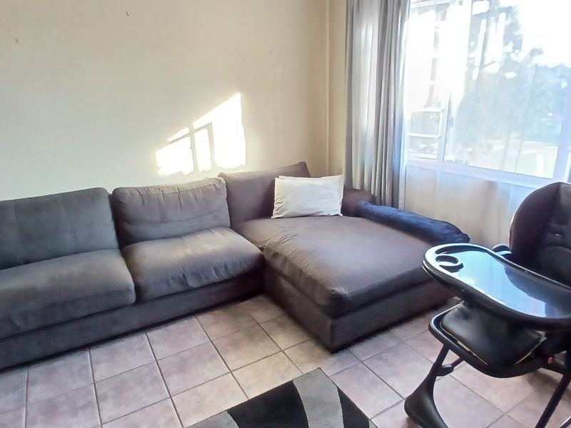 A living room area featuring tiled flooring and a large window, providing natural light to the space.