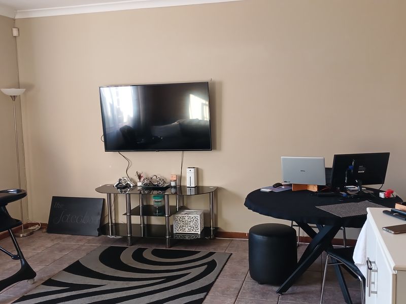 A living room area featuring tiled flooring and coved ceiling cornices, currently utilized as a multi-purpose living and workspace.