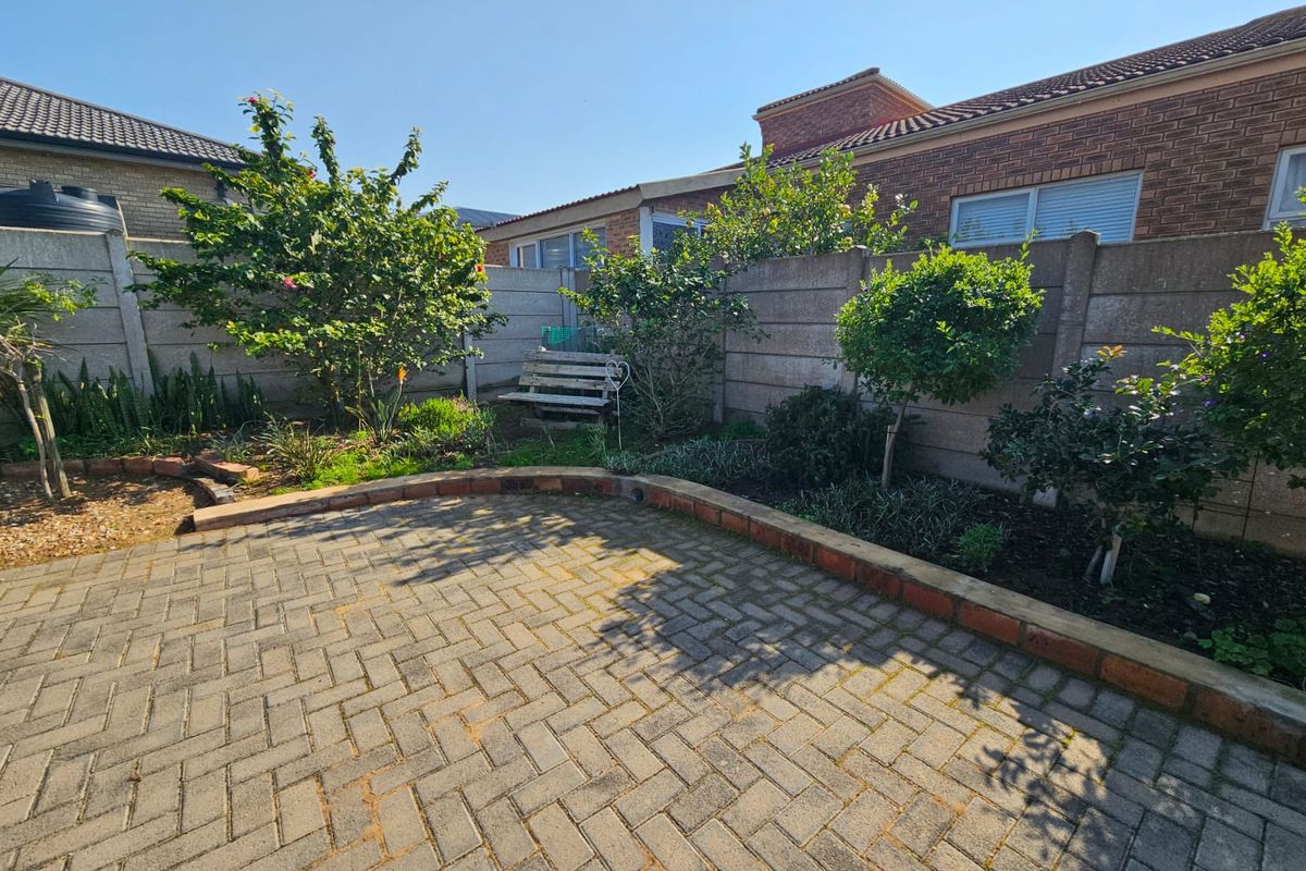 A private rear garden featuring a paved patio area, established landscaping, and secure precast concrete boundary walls.