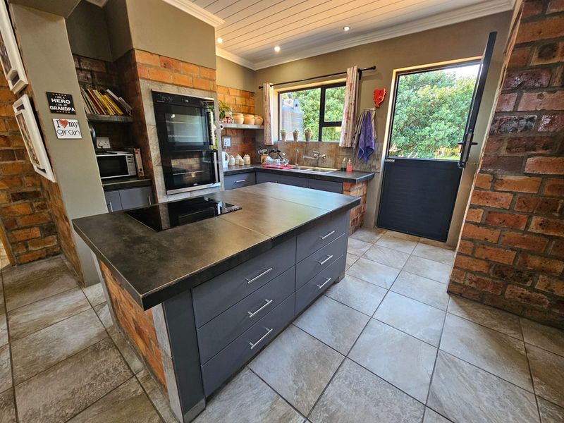 A rustic-style kitchen featuring exposed brick walls, a central island with an integrated hob, built-in oven, and direct access to the garden via a stable door.